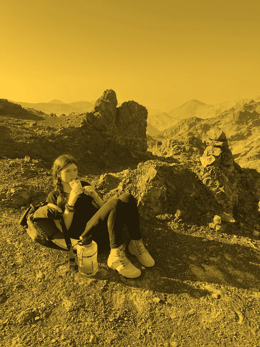 A student sits high on a cliff edge above the valley, looking out across the range, washed in Gold yellow