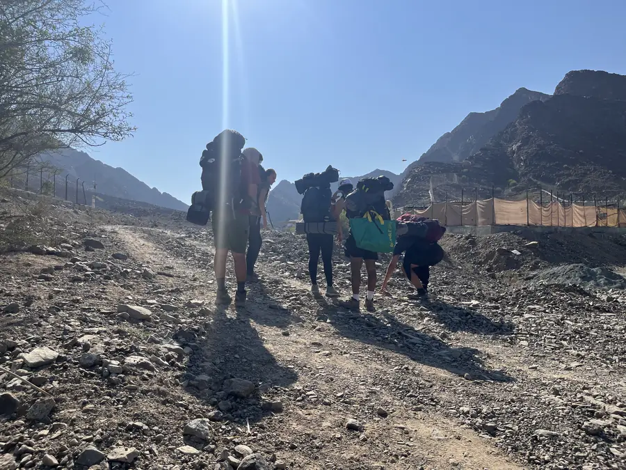 Two students shoulder their expedition packs at the head of a rocky wadi trail