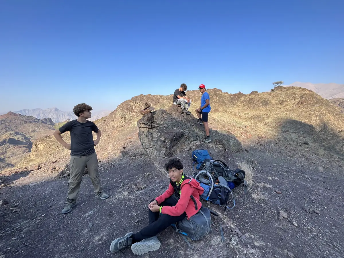Students rest on a rocky summit above the haze, packs down beside them