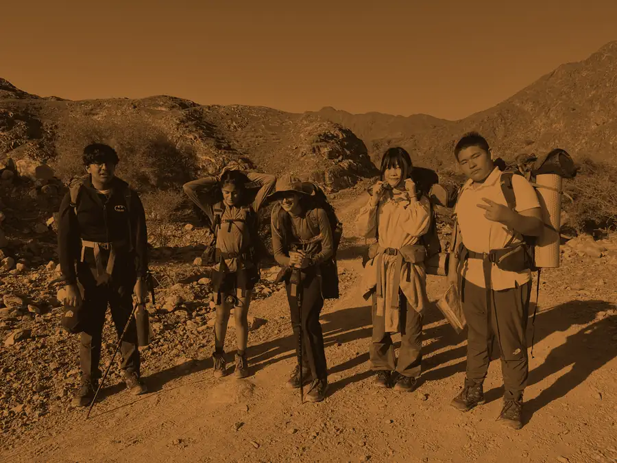 A Bronze expedition team pauses for a group photo on the trail, packs still on, washed in bronze