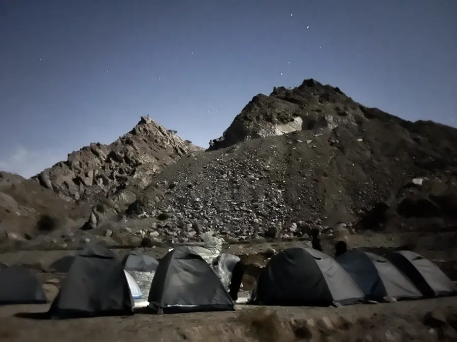 A row of expedition tents pitched below a rocky ridge at dusk